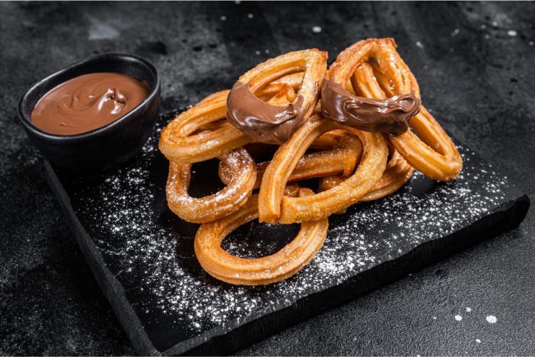 Churros on a slate board with chocolate dip on the side.