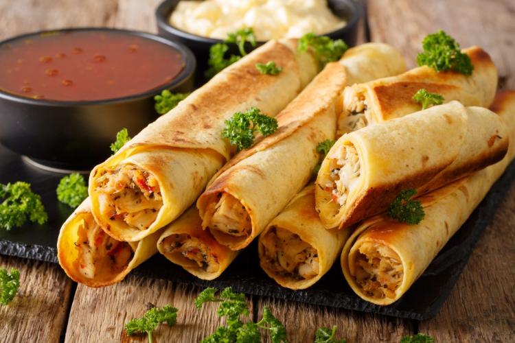A serving of baked chicken taquitos with tomato sauce and cheese sauce.