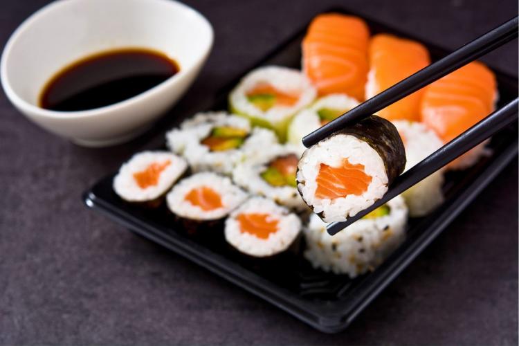 Chopsticks holding a single salmon sushi roll.