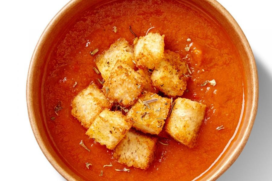 A bowl of gazpacho with croutons and herbs.