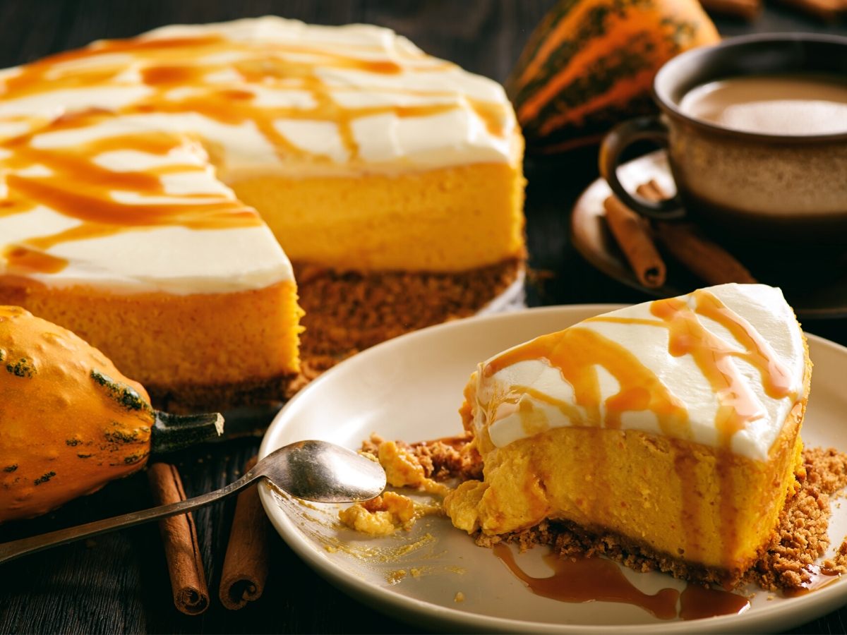 A plate with a slice of pumpkin cheesecake with the rest of the cake on the background.