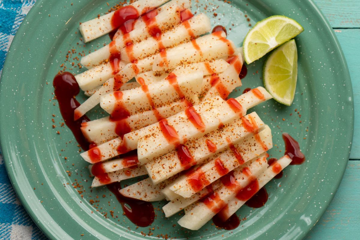A plate with jicama with chamoy sauce and chili powder, with tow lime wedges on the side.