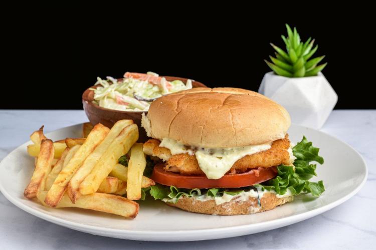 A baked haddock in breadcrumbs sandwich accompanied with fries and coleslaw.