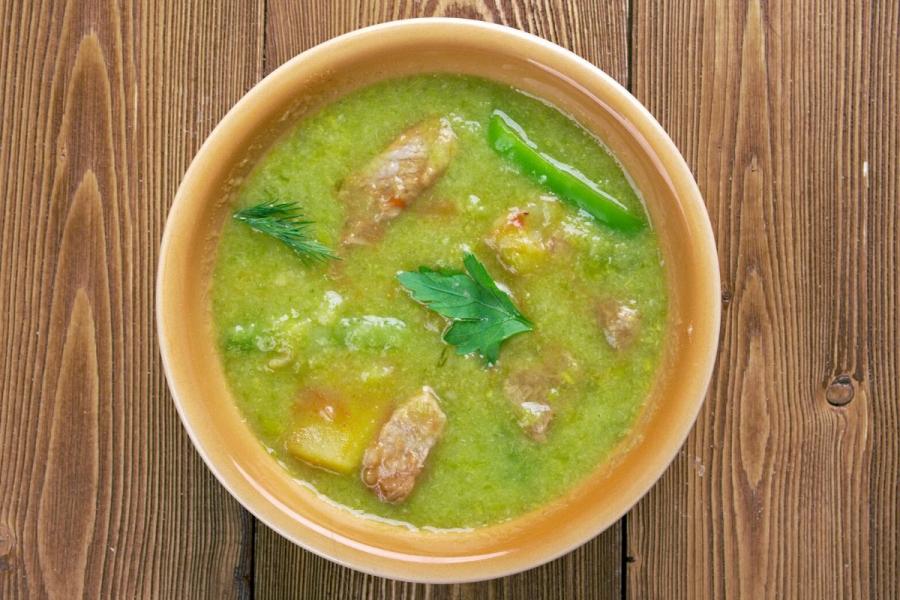 A steaming bowl of New Mexican green chile stew with tender chunks of pork and diced potatoes, granished with coriander.