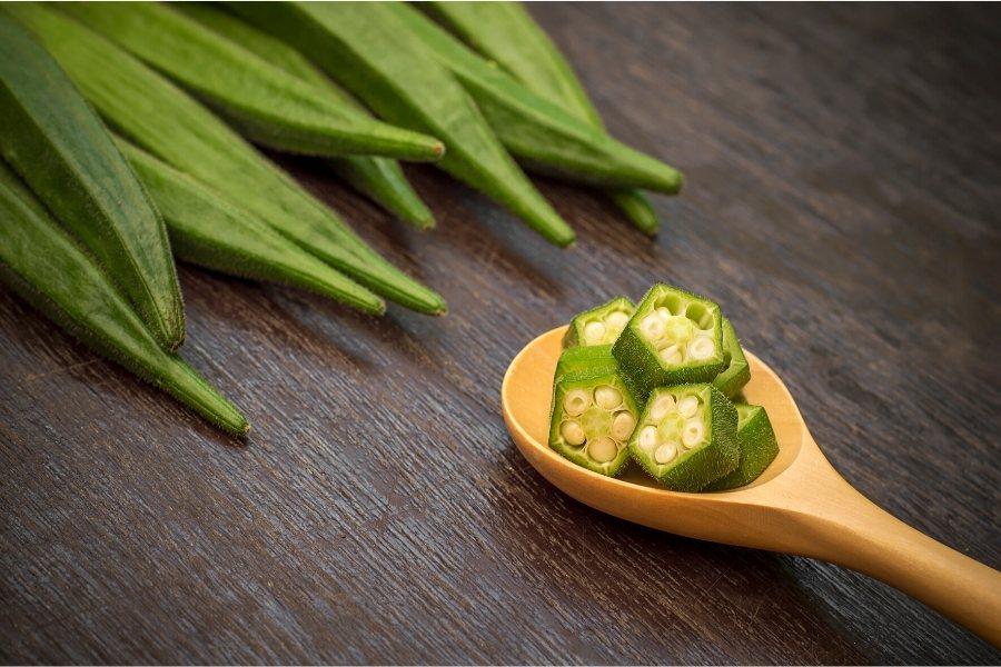 Fresh okra pods and a wooden spoon with chopped okra.