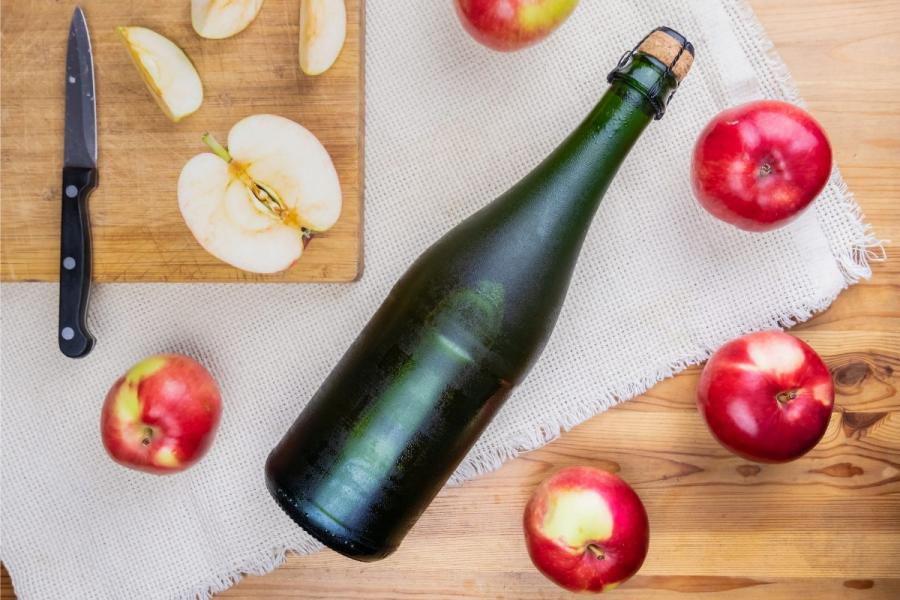 A bottle of cider, closed and chilled, surrounded by ripe apples.